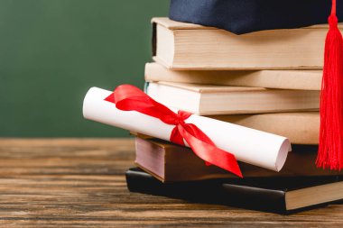 yeşil izole ahşap yüzey üzerinde kitap, akademik kap ve diploma