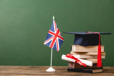 Yeşil üzerine izole ahşap yüzeyüzerinde kitaplar, akademik şapka, diploma ve İngiliz bayrağı