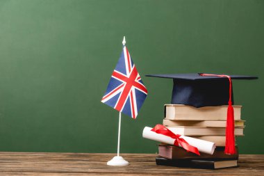 Books, academic cap, diploma and british flag on wooden surface isolated on green clipart