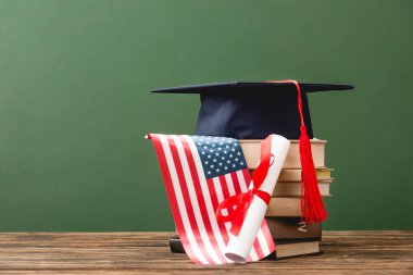 yeşil izole ahşap yüzeyüzerinde kitap, akademik kap, diploma ve Amerikan bayrağı