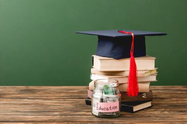 yeşil izole ahşap yüzeyüzerinde kitap, akademik kap ve kumbara