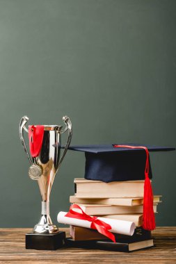 kitap, diploma, akademik kap, kupa kupası ve madalya ahşap yüzey üzerinde gri izole 