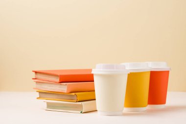 stack of books and colorful disposable cups on white surface isolated on beige clipart