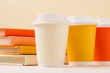 stack of books and colorful disposable cups on white surface isolated on beige clipart