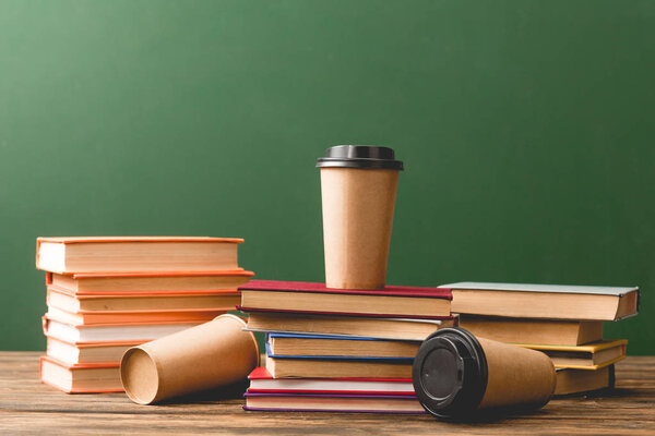 Books and disposable cups on wooden surface on green