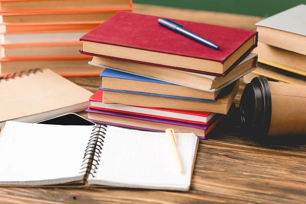 kitap, defter, kalem, akıllı telefon ve ahşap yüzey üzerindeki tek kullanımlık bardak yığınlarının seçici odak noktası 