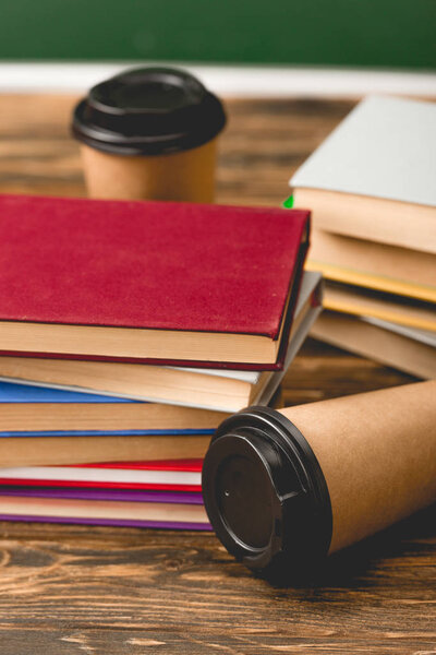 selective focus of books and disposable cups on wooden surface on green