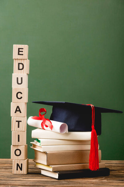 wooden blocks with letters, books, academic cap and diploma on wooden surface isolated on green