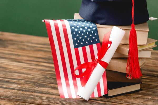 books, academic cap, diploma and american flag on wooden surface isolated on green