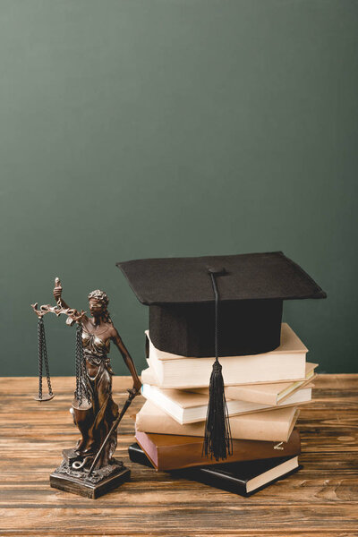 themis statuette, books and academic cap on wooden surface isolated on grey