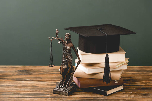 themis statuette, books and academic cap on wooden surface isolated on grey