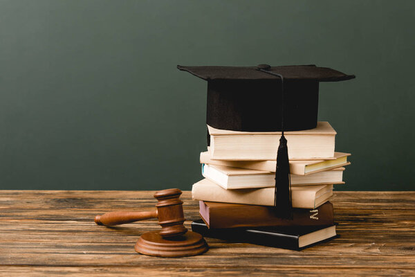 stack of books, academic cap and gavel on wooden surface isolated on grey