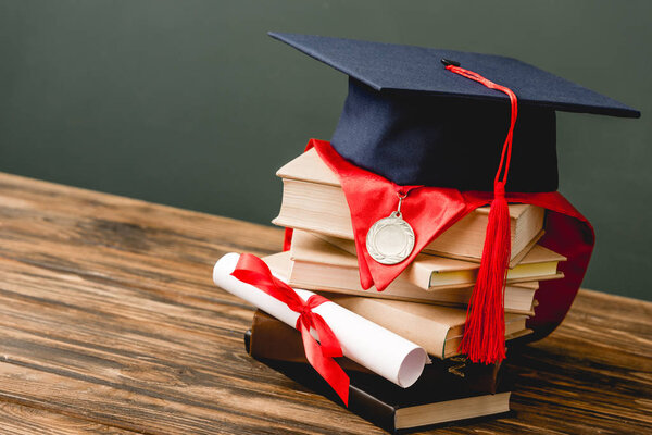 books, academic cap, medal and diploma on wooden surface isolated on grey