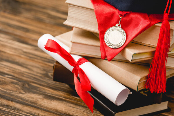 academic cap, books, medal and diploma on wooden surface