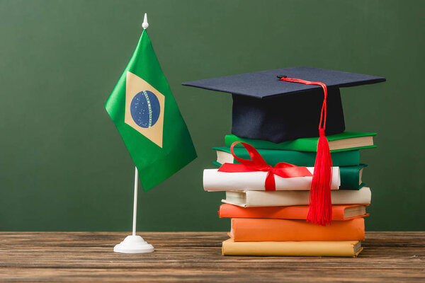 books, academic cap, diploma and brazilian flag on wooden surface isolated on green