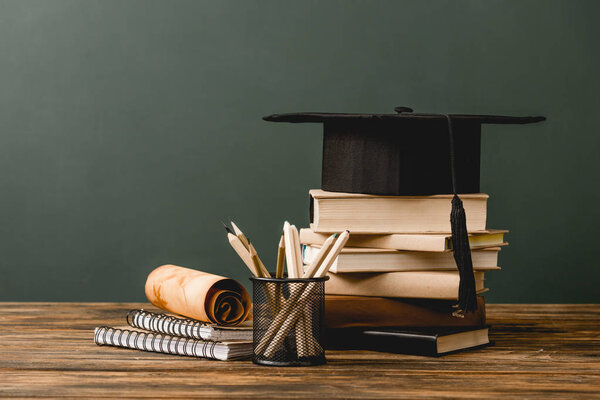 books, academic cap, notebooks, scroll, pencils on wooden surface isolated on grey