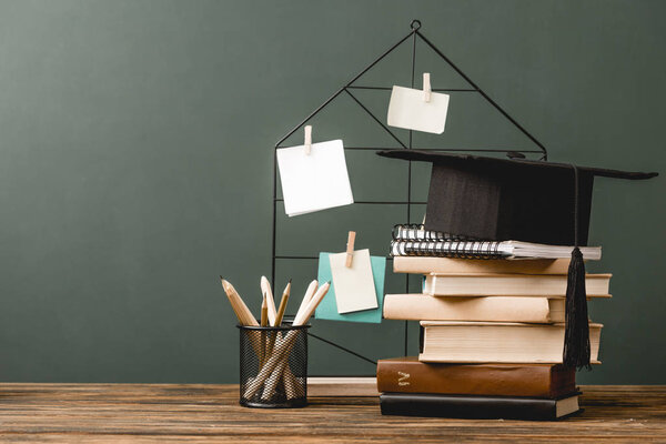 books, notebooks, academic cap, pencils and pinboard on wooden surface isolated on grey