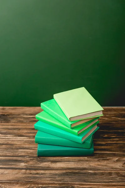 一叠五颜六色的书在木制表面隔离在绿色 — 图库照片