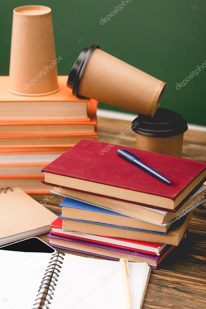 selective focus of books, notebooks, pens, smartphone and disposable cups on wooden surface on isolated on green