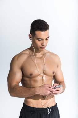 yakışıklı sportif karışık ırk adam kulaklık akıllı telefon tutan ve beyaz müzik dinleme