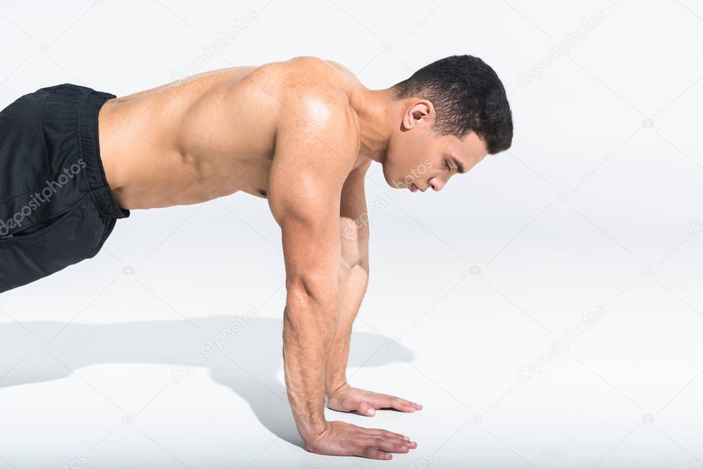 handsome sportive mixed race man doing push ups on white