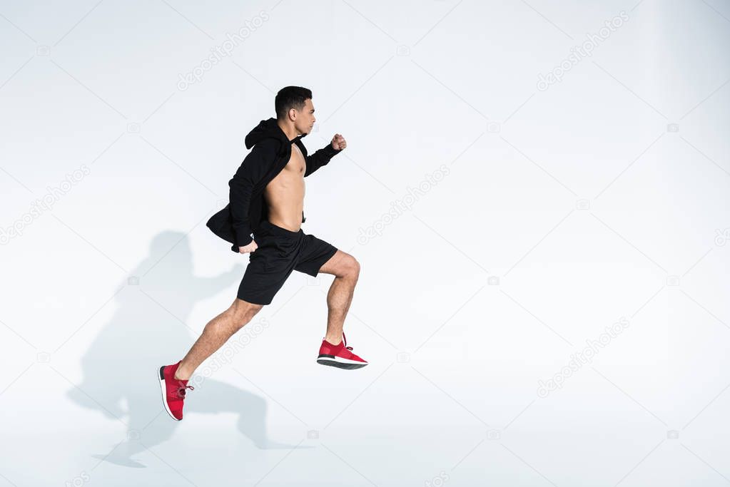 side view of sportive mixed race man in black sportswear running on white