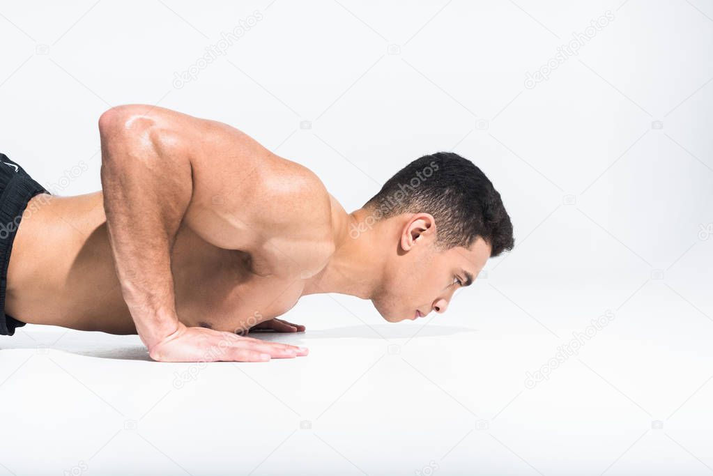 handsome mixed race man with muscular torso doing push ups on white