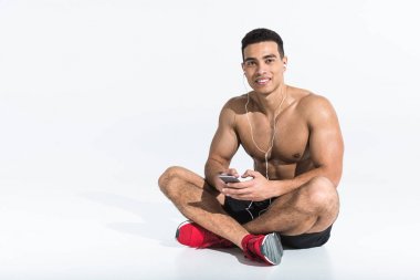 sportif karışık ırk adam çapraz bacaklar ile oturan ve beyaz kulaklıkmüzik dinleme