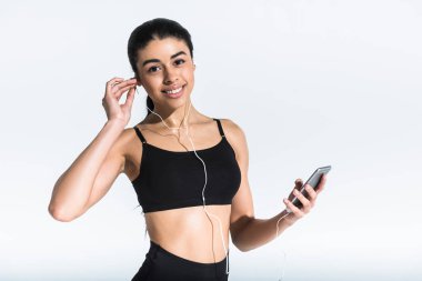 pretty smiling african american girl in black sports bra listening music in earphones on white clipart
