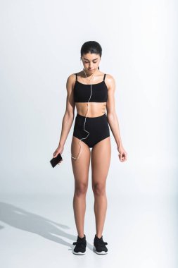 oldukça sportif afro-amerikan kız akıllı telefon tutan ve beyaz kulaklık müzik dinleme