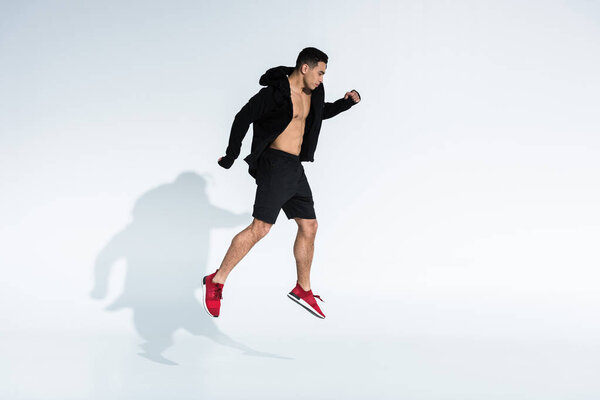 handsome mixed race man in black sports jacket, shorts and red sneakers jumping on white