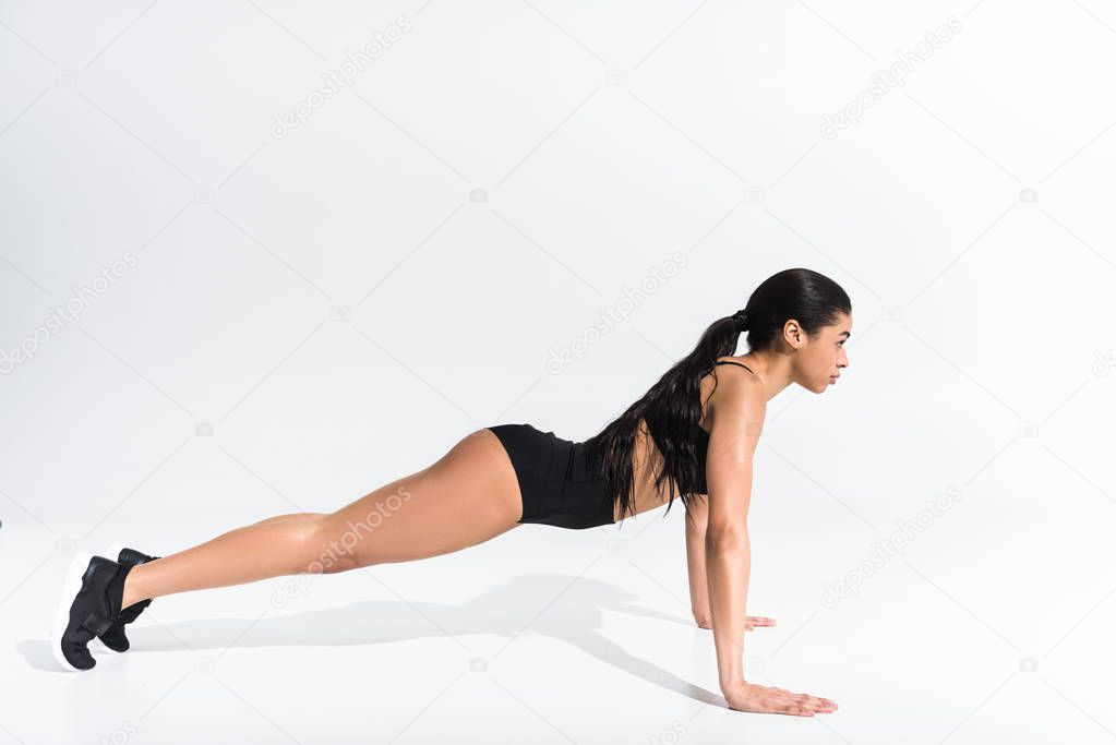 side view of sportive african american girl doing push ups on white background