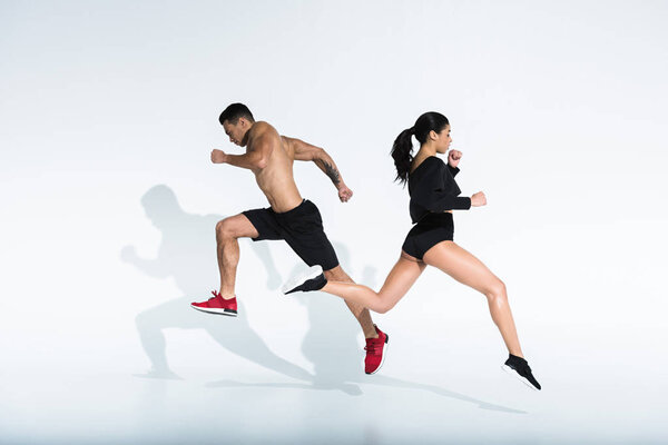 sportive african american girl and athletic mixed race man running on white background