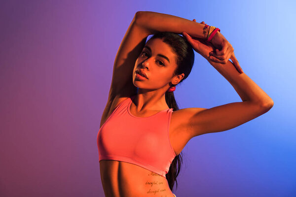 attractive sportive african american girl in pink sports bra posing on purple and blue gradient background