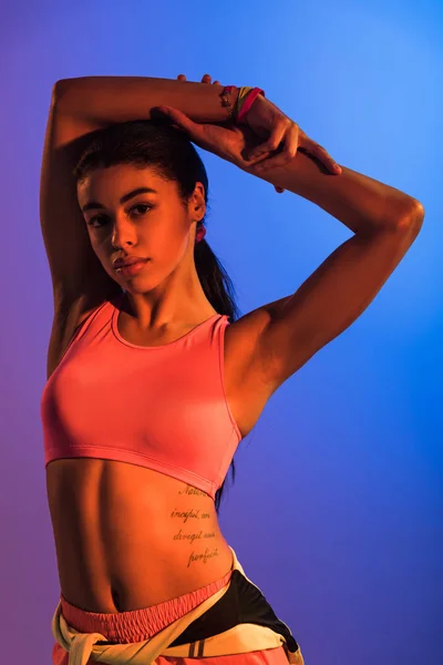 紫と青のグラデーションの背景にカメラでポーズピンクのスポーツブラジャーで美しい運動アフリカ系アメリカ人の女の子 — ストック写真
