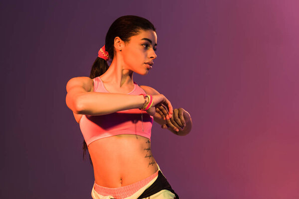 beautiful sportive african american girl warming up on purple background