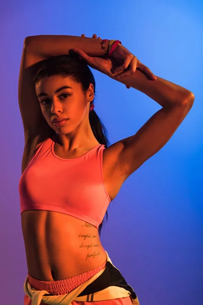 Beautiful athletic african american girl in pink sports bra posing at camera on purple and blue gradient background — Stock Image Beautiful Athletic African American Girl Pink Sports Bra Posing Camera Royalty Free Stock Images