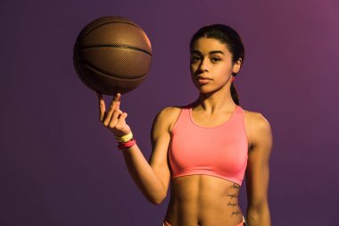 pembe spor sütyen güzel afro-amerikan kız kahverengi top tutan ve mor arka plan üzerinde kamera bakıyor
