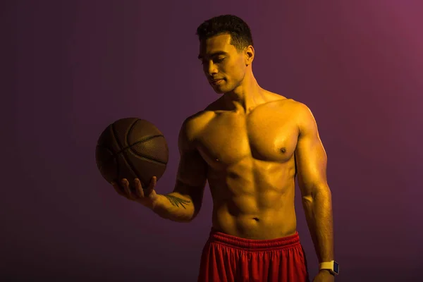 Pohledný Sportovní Muž Držící Hnědou Kouli Purpurovém Pozadí — Stock fotografie