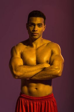 yakışıklı sportif karışık ırk adam mor arka plan üzerinde çapraz kolları ile kamera poz