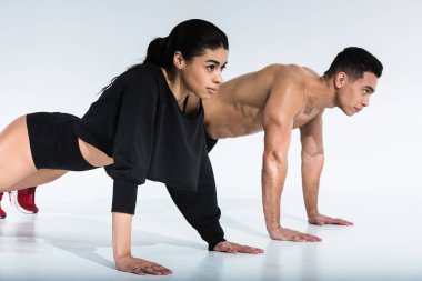 sportive multicultural woman and man doing push ups on white background clipart