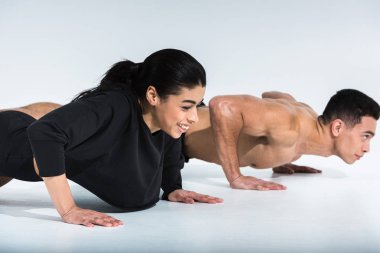 smiling african american girl and mixed race man doing push ups on white clipart