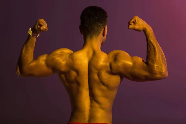 运动男子与肌肉躯干在紫色背景显示二头肌的背面视图 — 图库照片