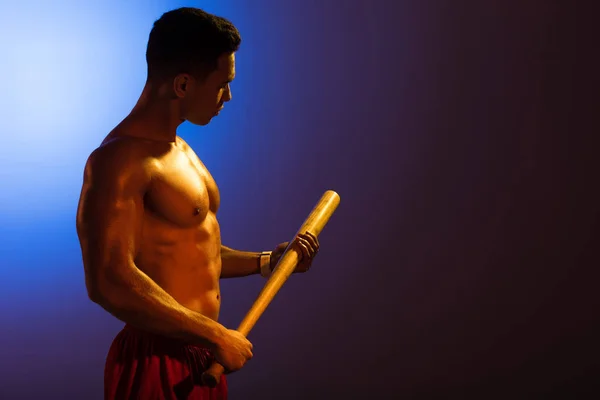 运动无衬衫混合种族男子拿着棒球棒的蓝色和深紫色梯度背景 — 图库照片