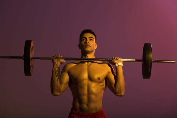 handsome athletic mixed race man lifting barbell on purple background