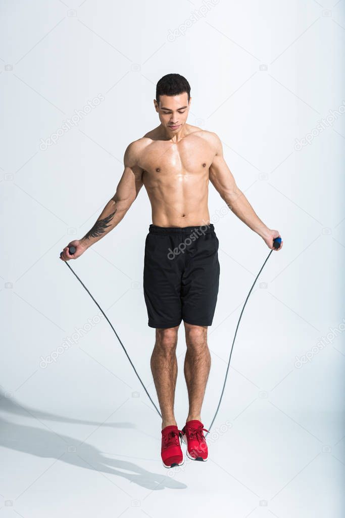 handsome sportive mixed race man jumping with skipping rope on white