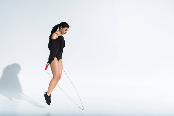 attractive sportive african american girl jumping with skipping rope on white