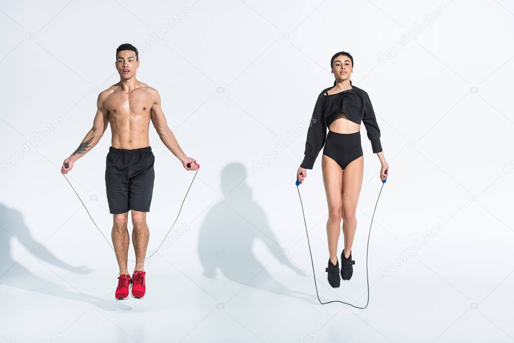 sportive multicultural woman and man jumping with skipping ropes on white