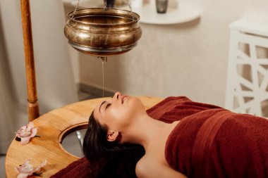 ayurvedik işlem sırasında shirodhara gemi altında yatan rahat genç kadın