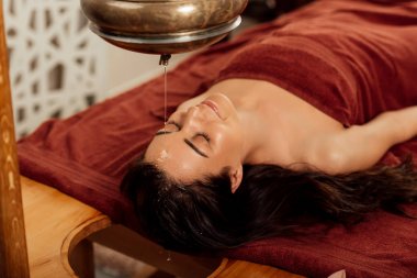 ayurvedik işlem sırasında shirodhara gemi altında yatan rahat genç kadın